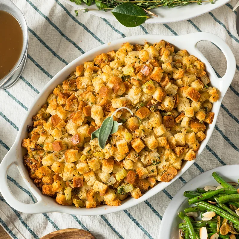 A dish of classic Thanksgiving stuffing on a white tablecloth with green stripes