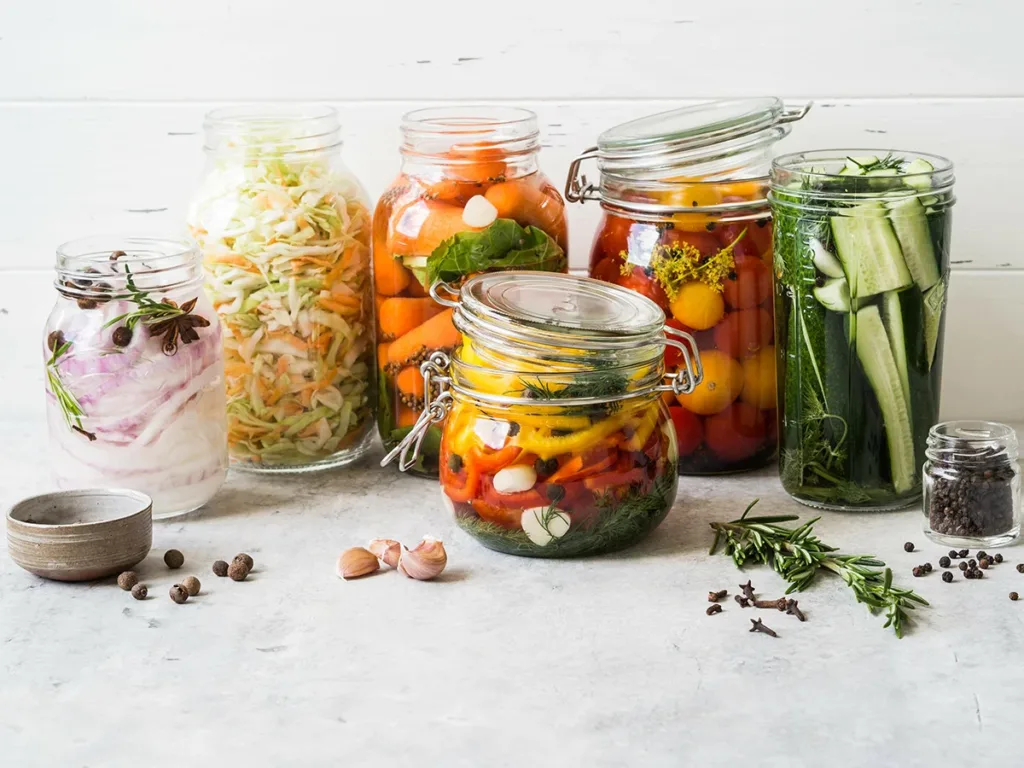 Jars of pickled and fermented vegetables against a white background, showing the concept of the best foods for gut health